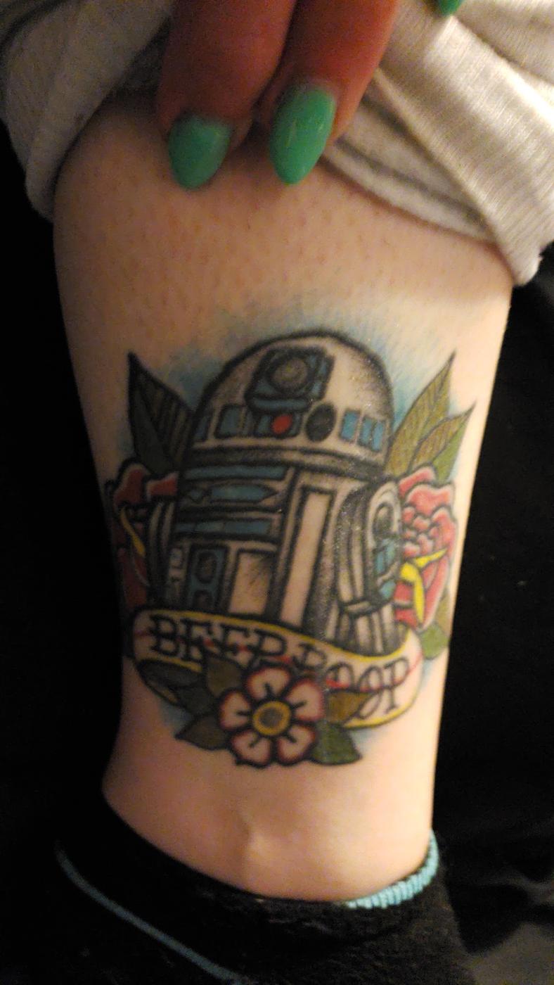 A color tattoo of R2-D2 surrounded by flowers, on a forearm