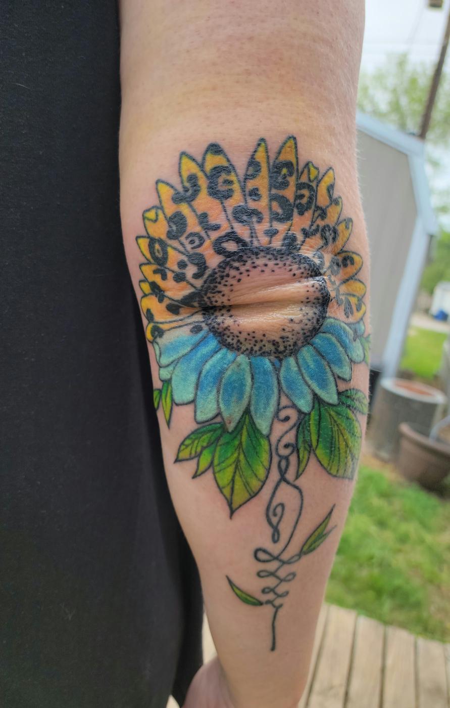 A color sunflower with a ringed planet at its center, tattooed around an elbow